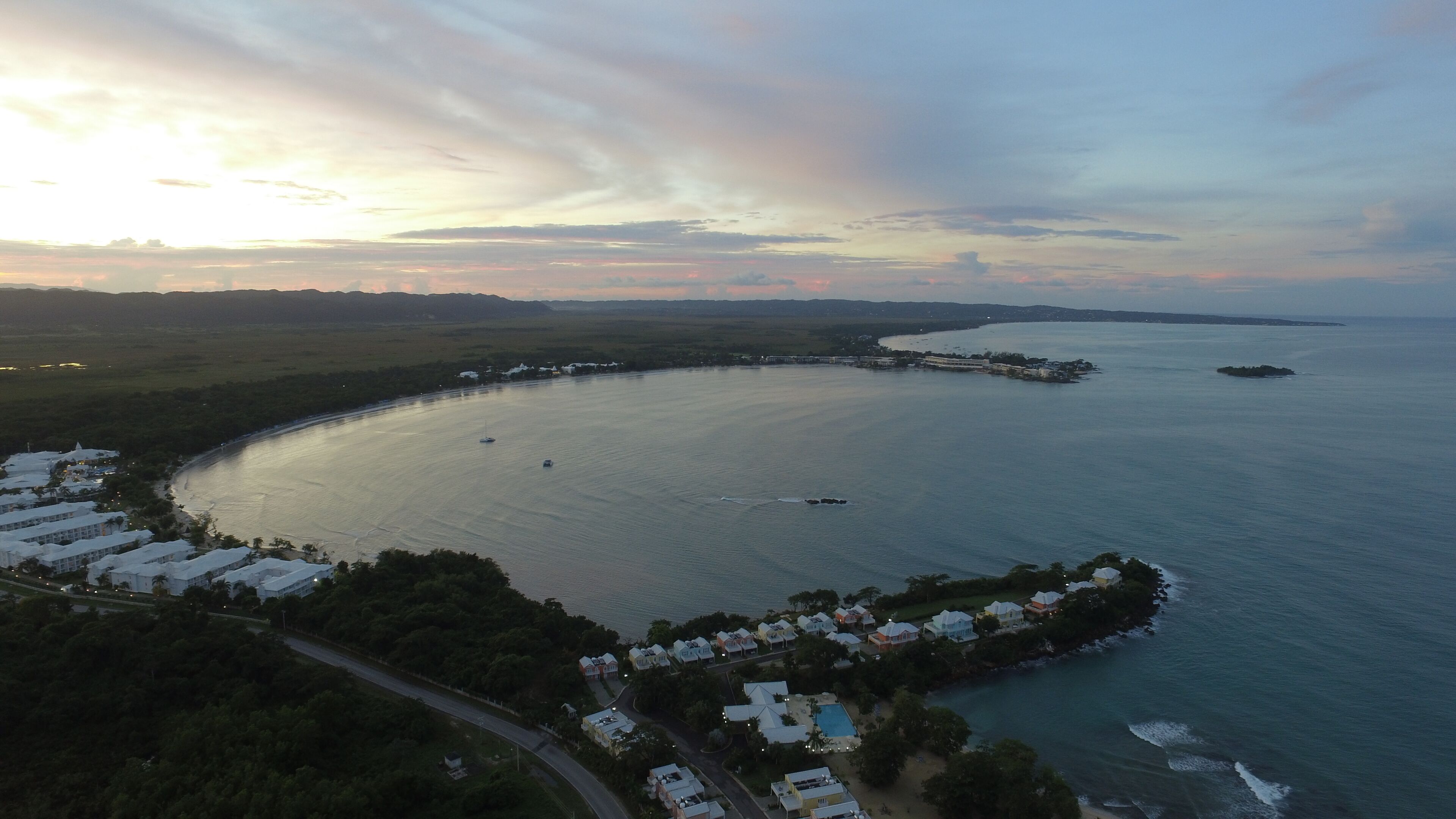 An aerial view of a coastal resort with a marina, beachfront villas, and a large body of water.