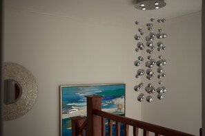 A staircase with a wooden handrail, a wall-mounted abstract painting, and a decorative hanging of spherical objects.
