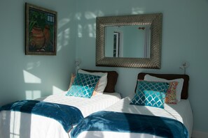 A bedroom with two beds, a large mirror, and a painting on the wall.