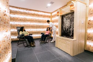 A room with wooden walls, two reclining chairs, a wooden cabinet, and a large window with a view of trees.