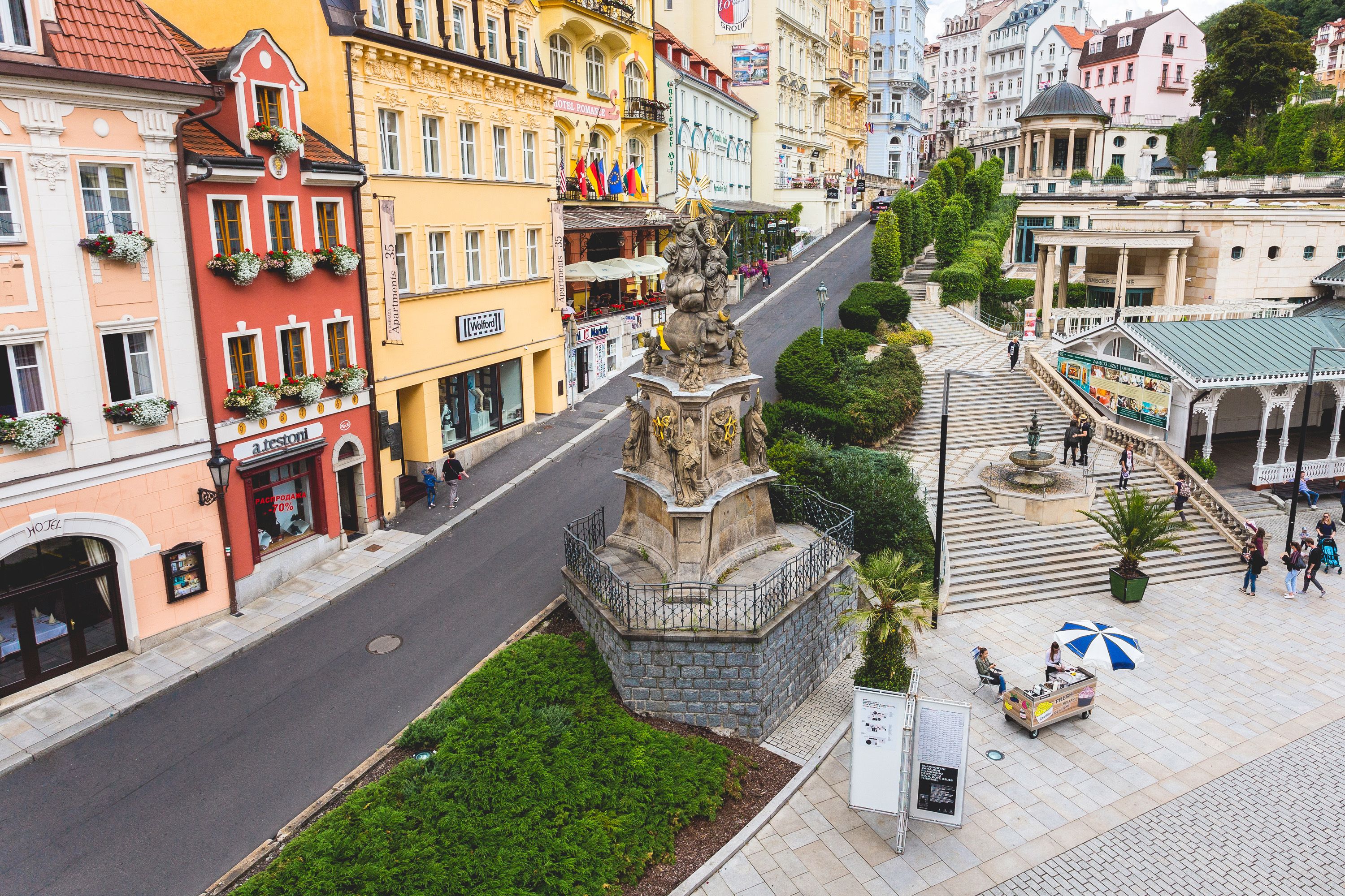 A square with a central monument, surrounded by colorful buildings and a street.
