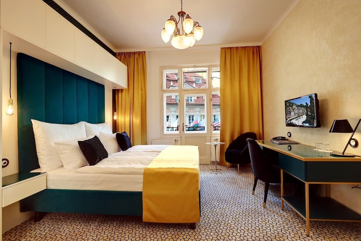 Ein Hotelzimmer mit Bett, Schreibtisch, Stuhl, Fernseher und einem fensterbepflanzten Fenster.