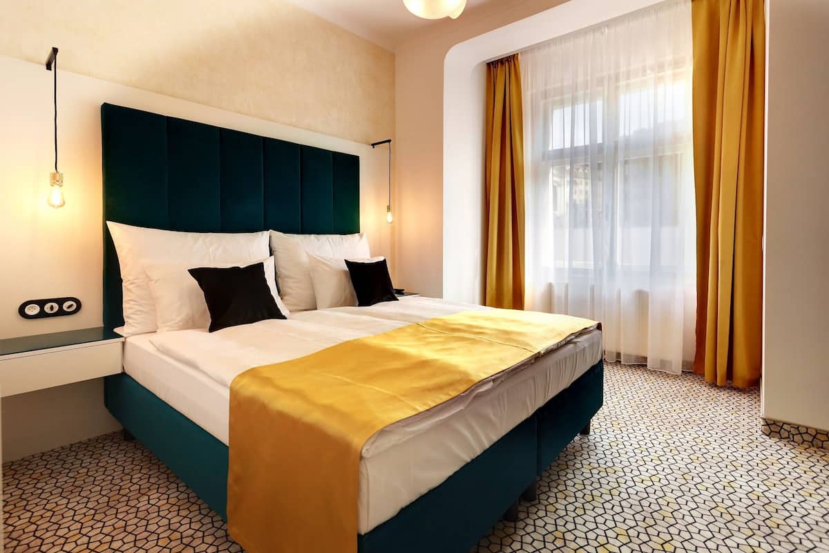 Ein Hotelzimmer mit Bett, Nachttisch, Wandlampe und einem Fenster mit Vorhängen.