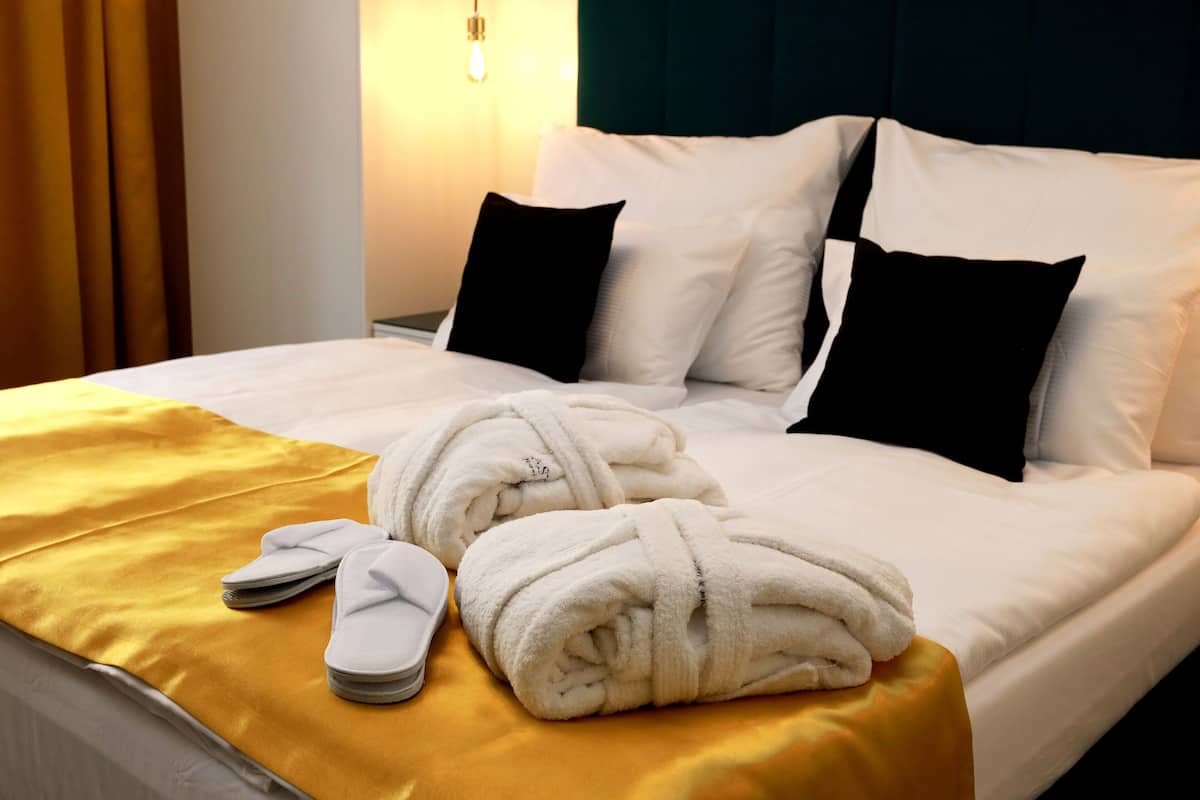 Ein ordentlich gemachtes Bett mit weißen und schwarzen Kissen, einer gelben Decke und einem Paar weißer Hausschuhe.