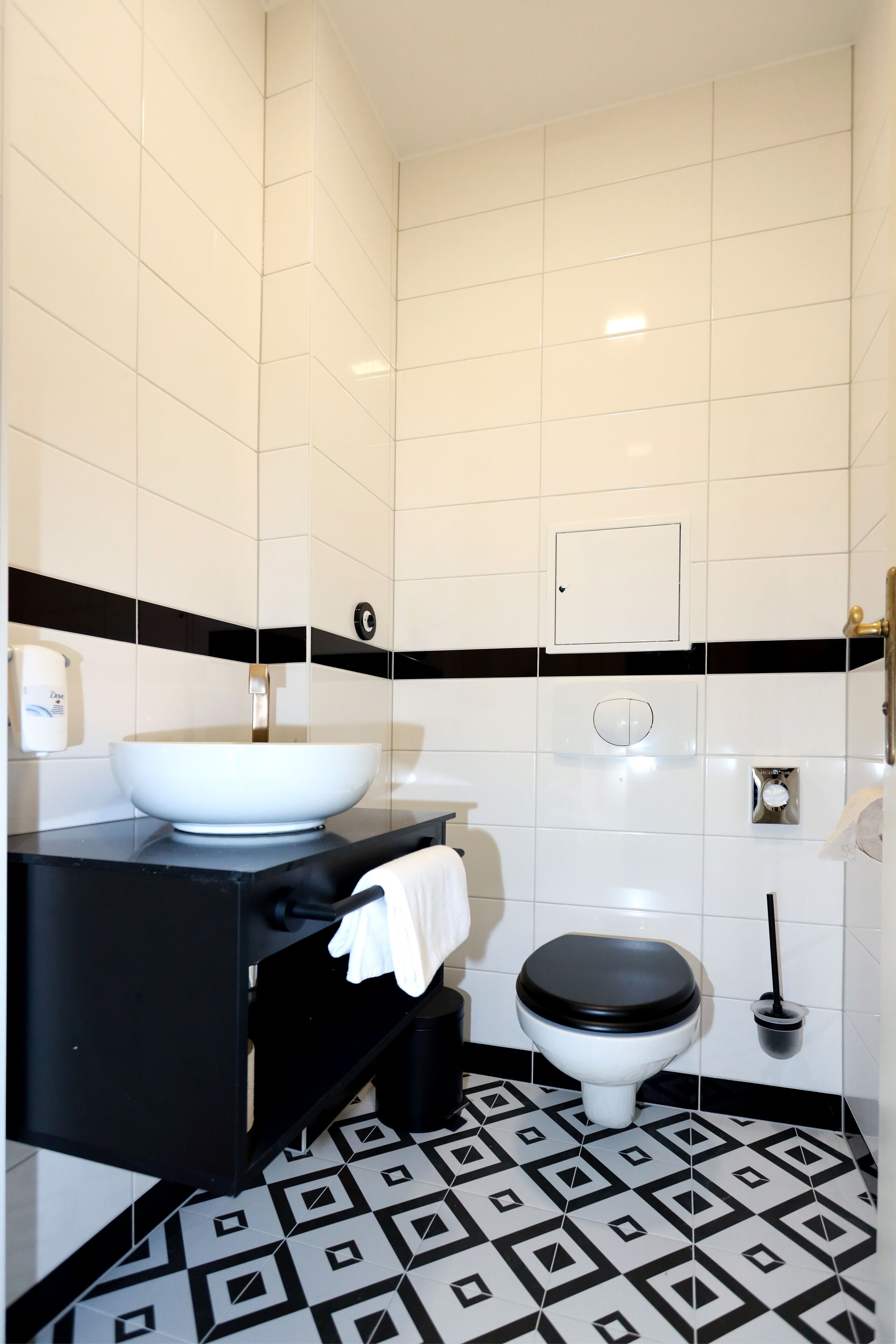 A bathroom with a white sink, black countertop, and a toilet with a black seat. The floor has a black and white geometric pattern.
