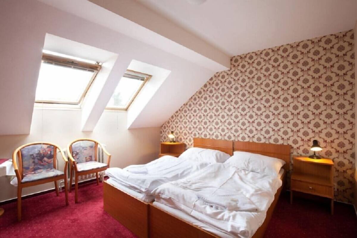 A bedroom with a bed, two chairs, a nightstand, and a patterned wall.