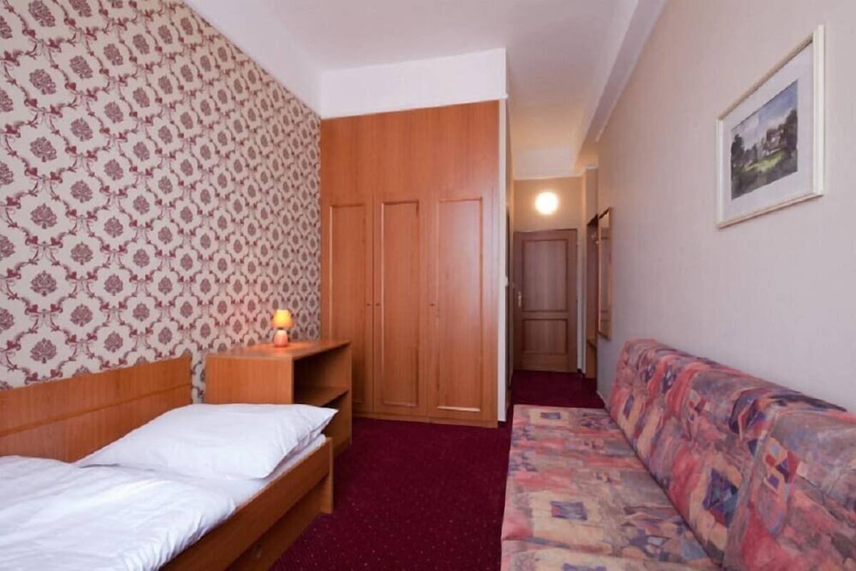 A bedroom with a bed, a nightstand, a wooden wardrobe, a sofa, and a framed picture on the wall.