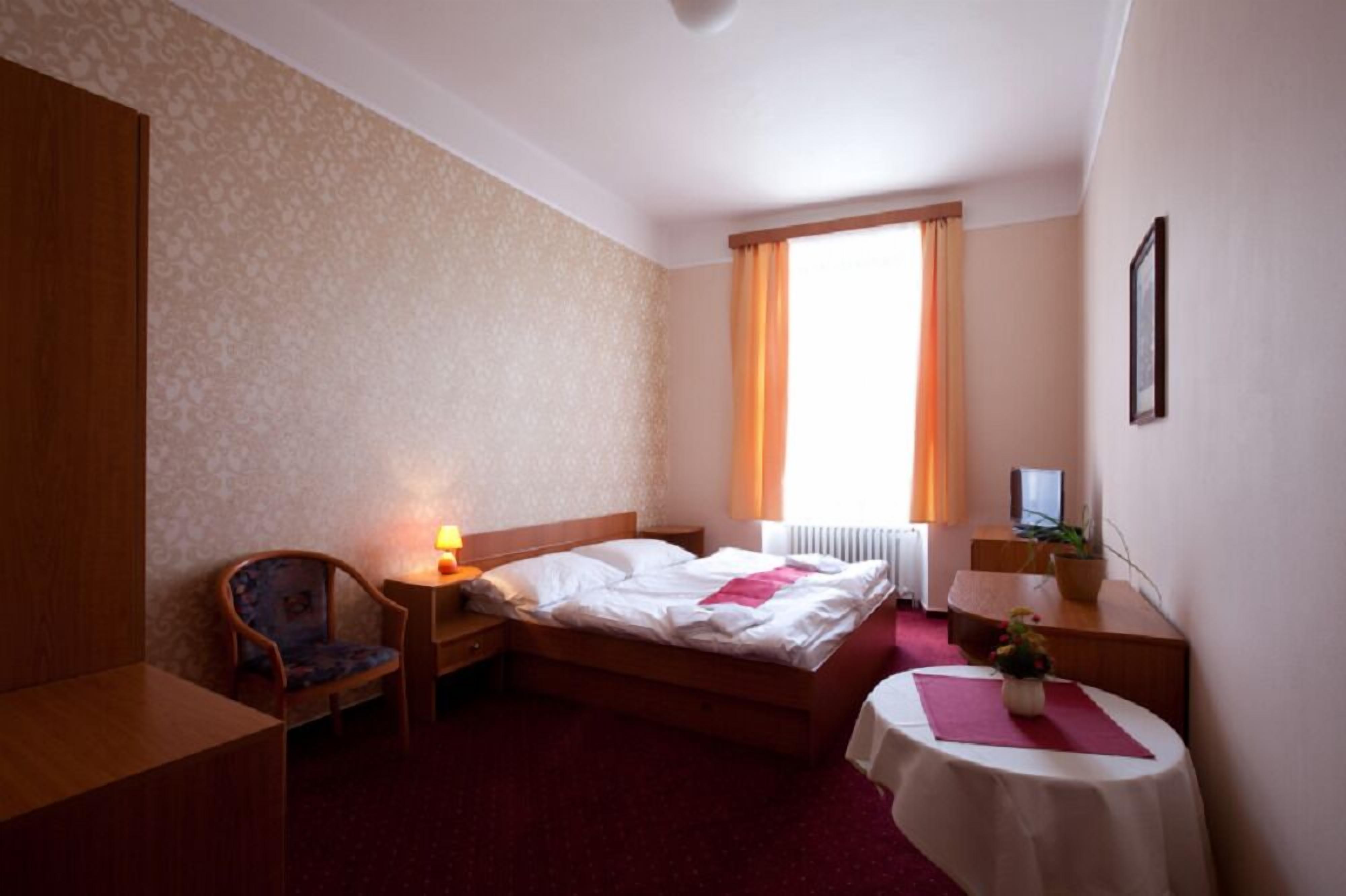 A hotel room with a bed, a chair, a desk, a table, a TV, and a window with curtains.