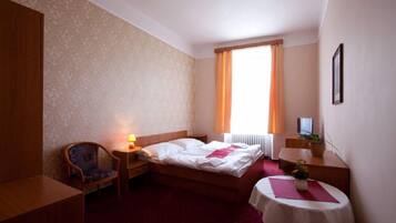 A hotel room with a bed, a chair, a desk, a table, a TV, and a window with curtains.