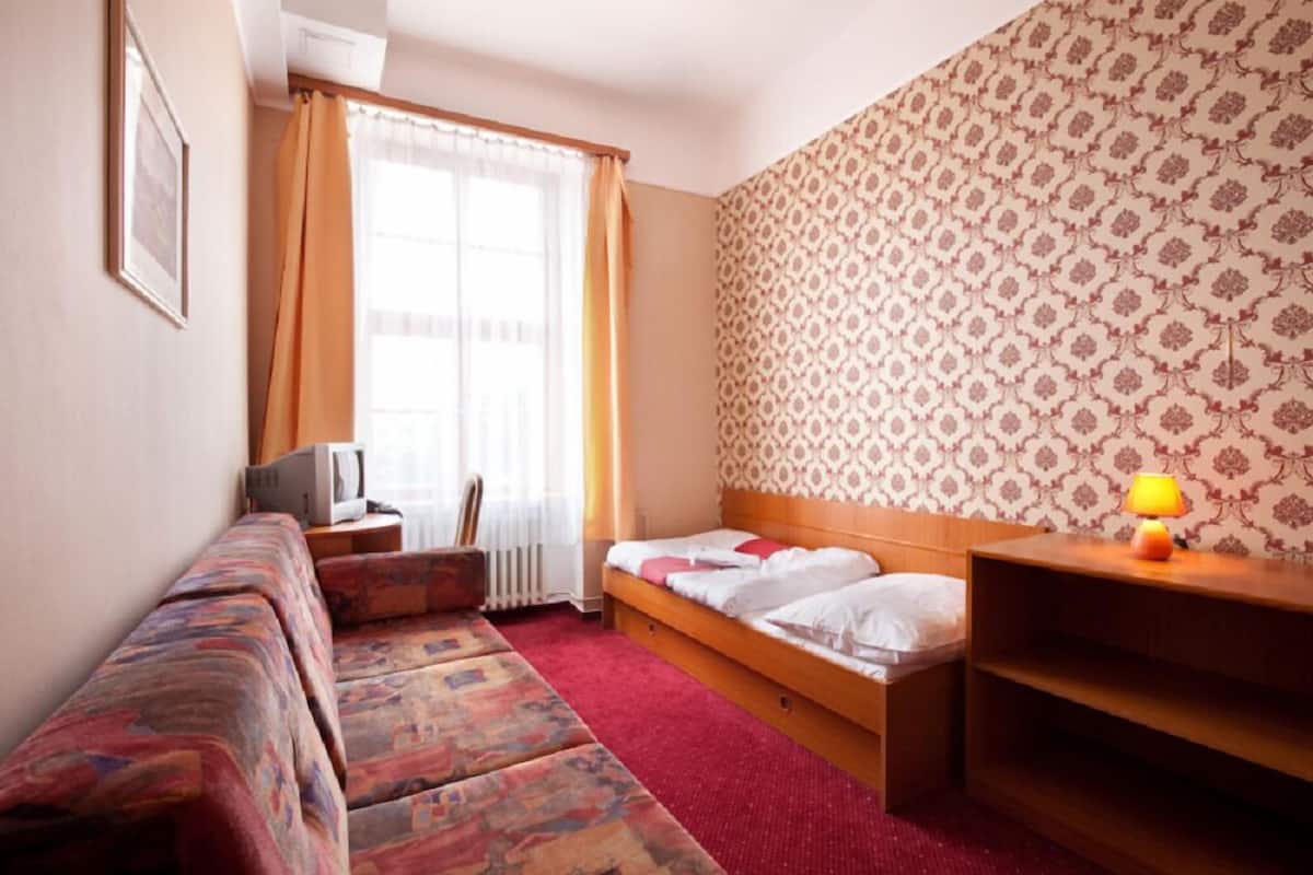 A small hotel room with a bed, a sofa, a TV, and a lamp.
