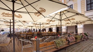 An outdoor café with multiple tables and chairs under large umbrellas with a logo. - Hotel U Černého orla (Telc)