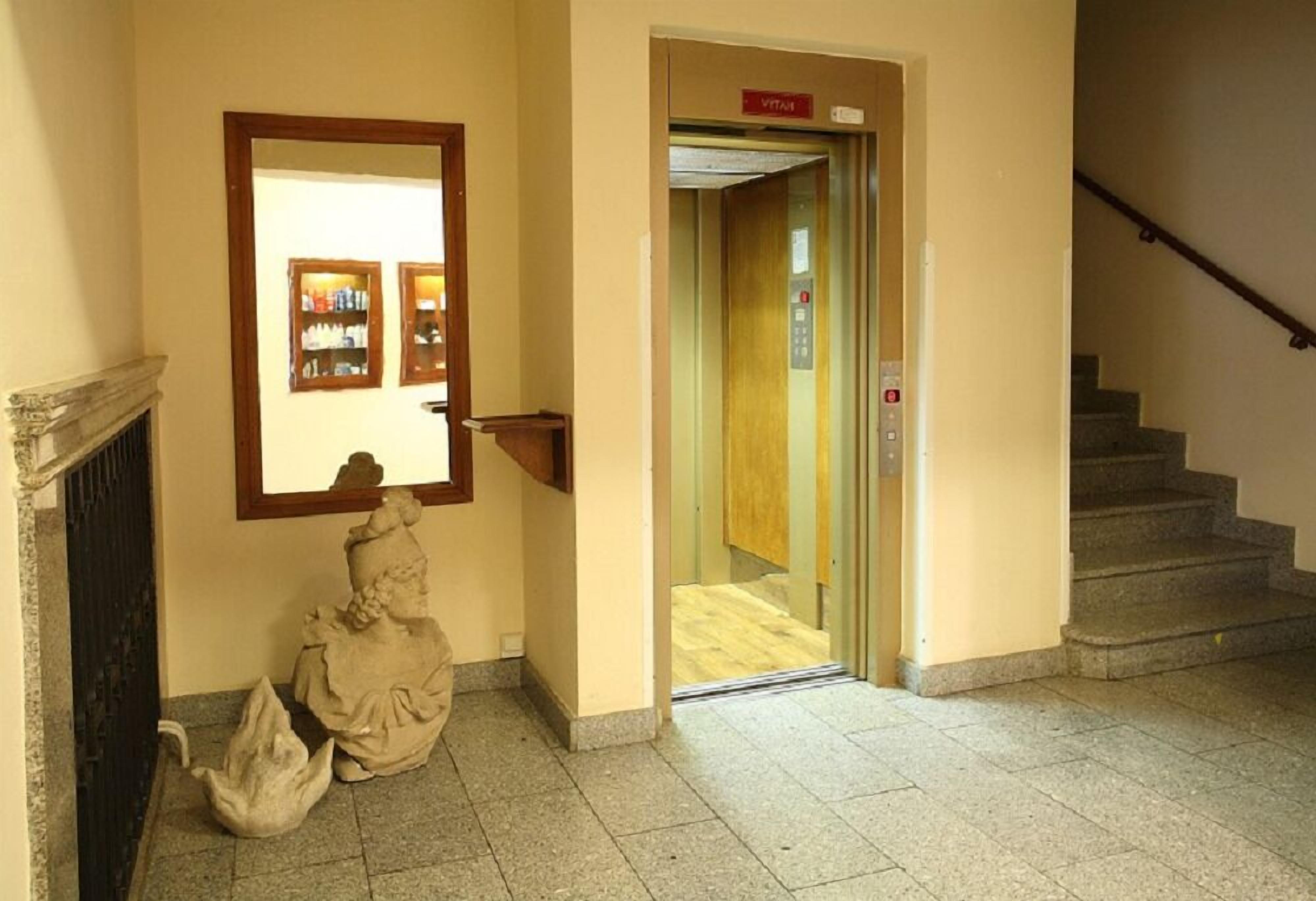 En gang med en marmorstatue, et spejl, en reol og en elevator.