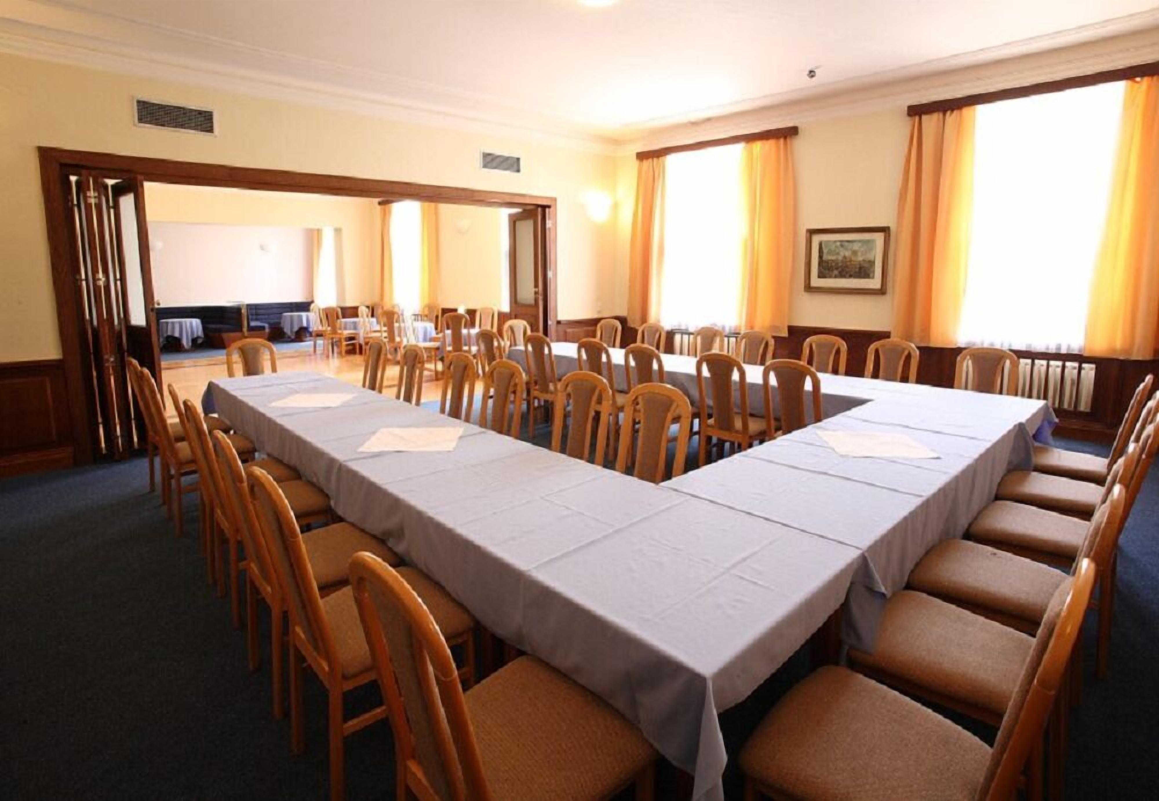 Une salle de conférence avec une longue table et des chaises, de grandes fenêtres avec des rideaux et un tableau accroché au mur.