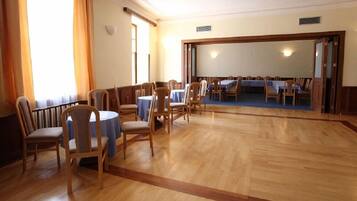 A room with wooden flooring, multiple tables with blue tablecloths, and wooden chairs.
