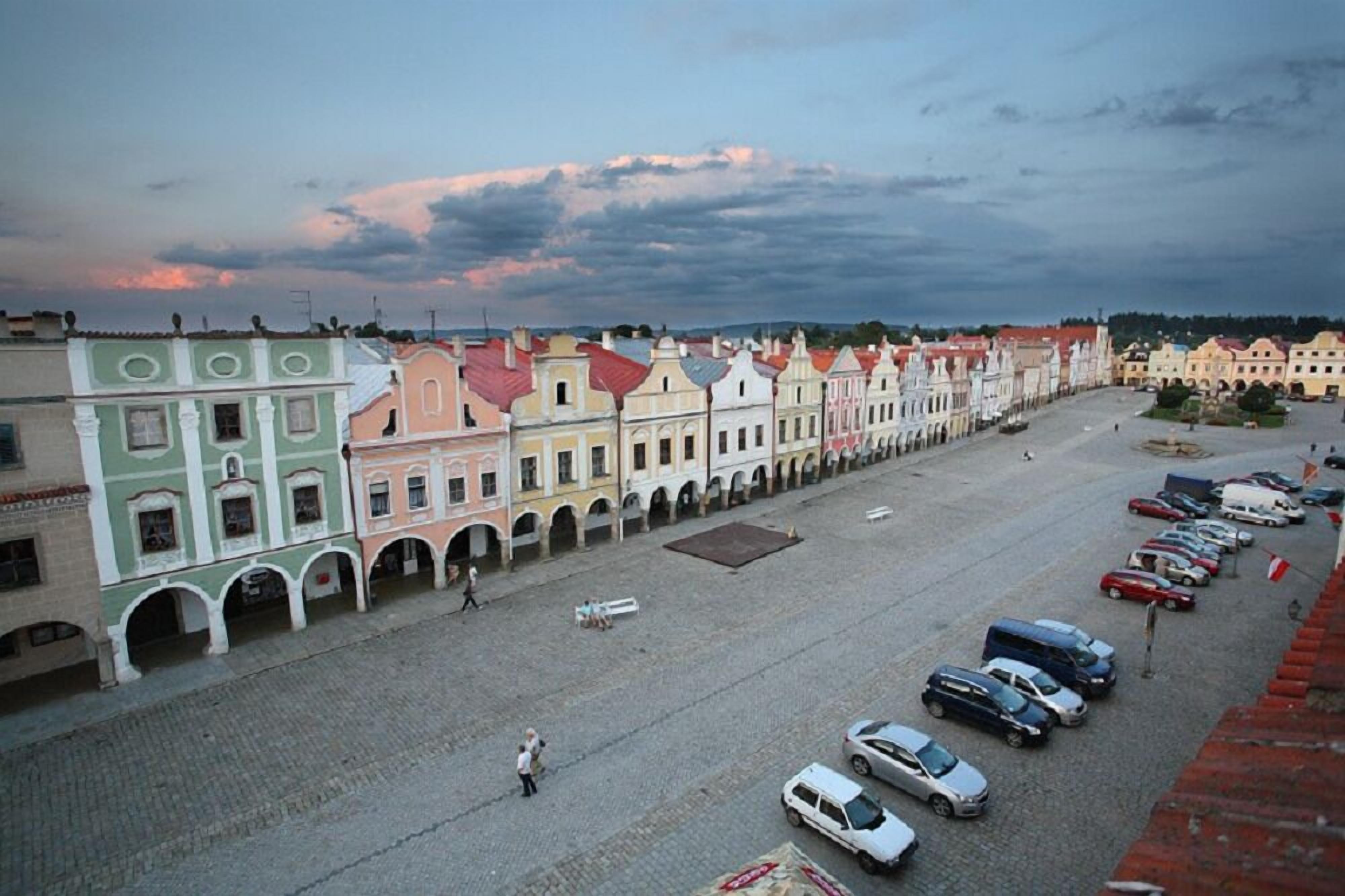 A historic street with colorful buildings, a paved square, and parked cars.