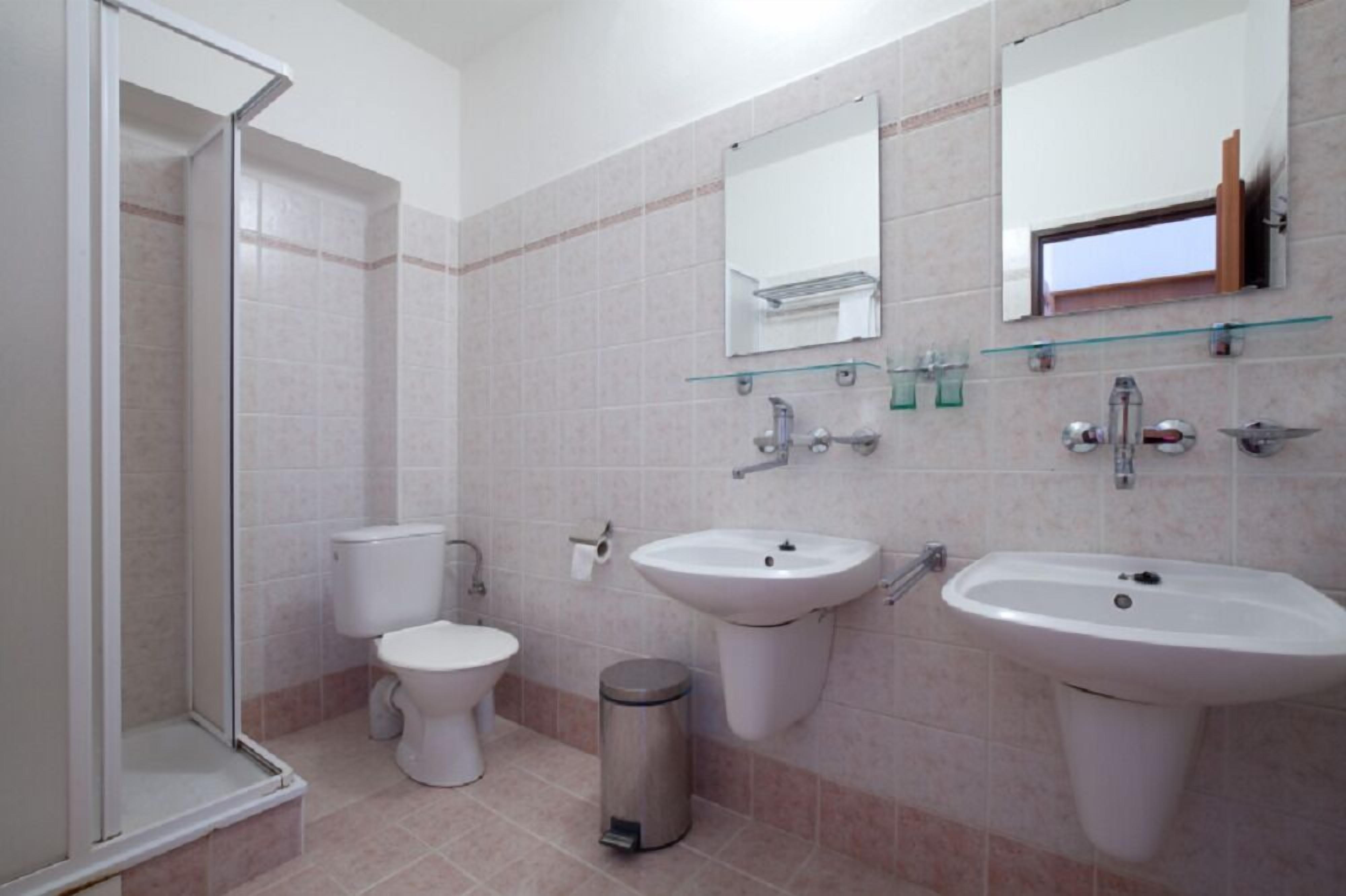 A modern bathroom with a glass shower enclosure, two sinks, a toilet, and a trash can.