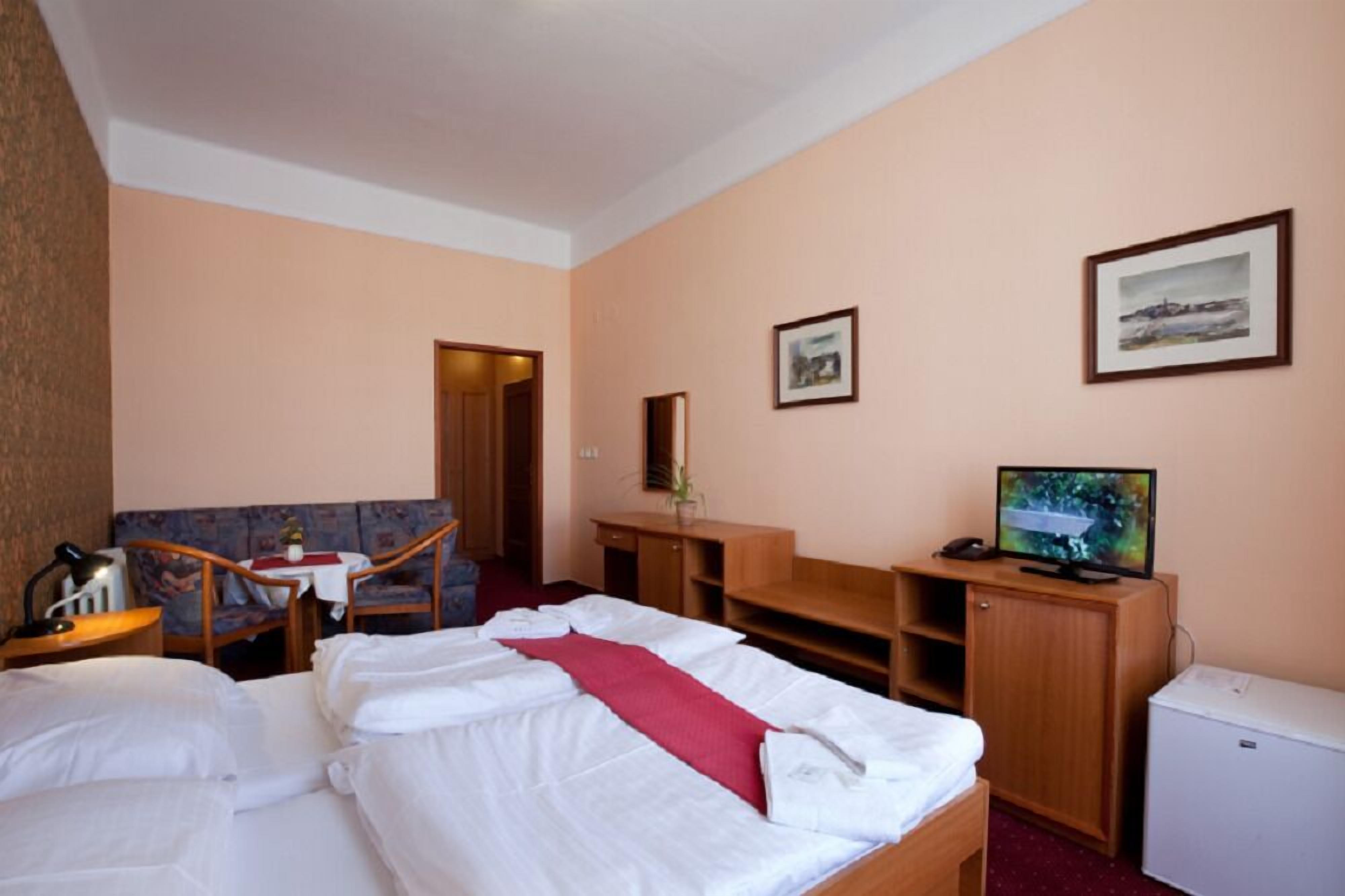 A hotel room with two beds, a desk, a television, and a small refrigerator.