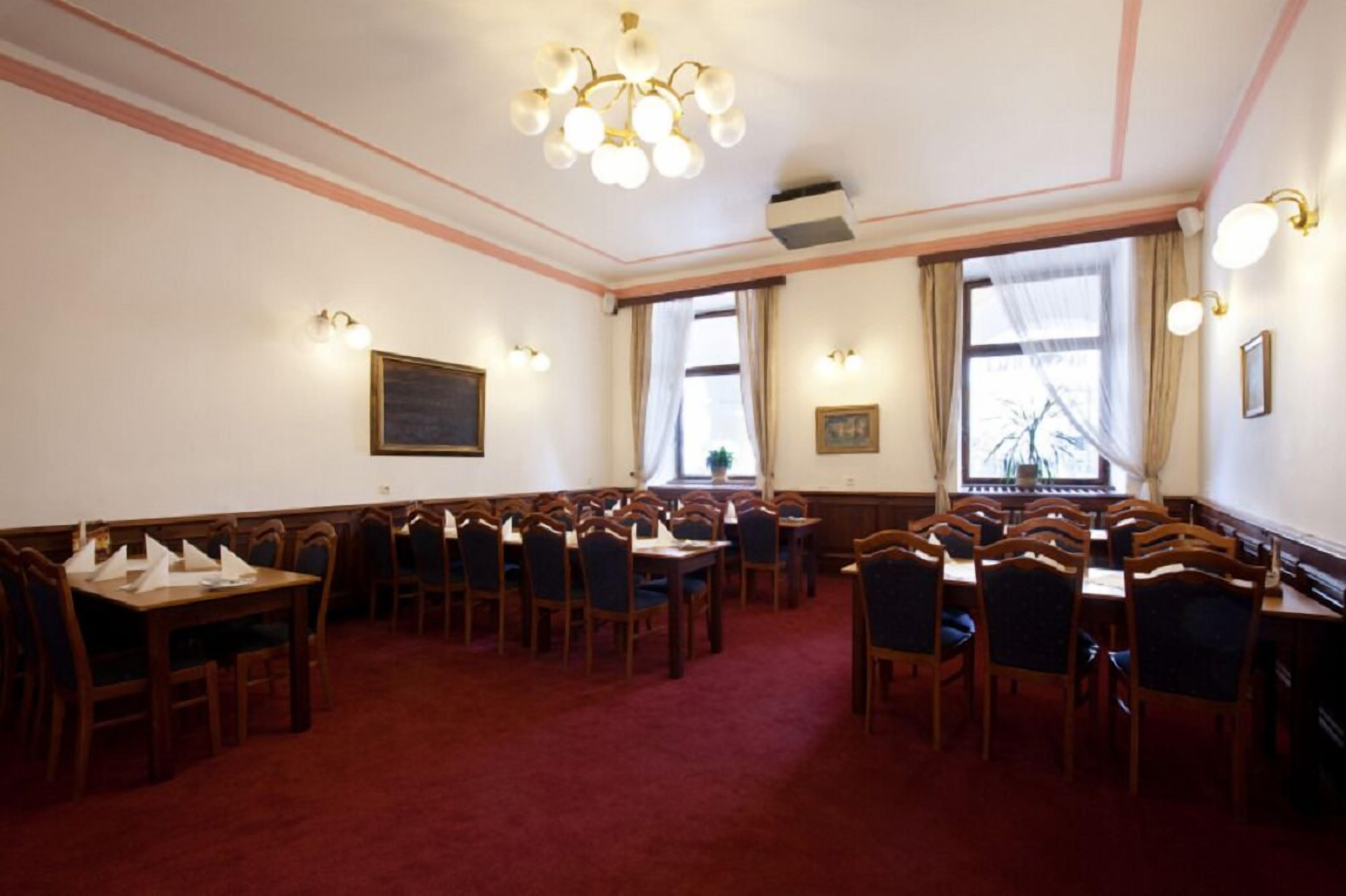A conference room with wooden tables and chairs, a chandelier, and large windows with curtains.
