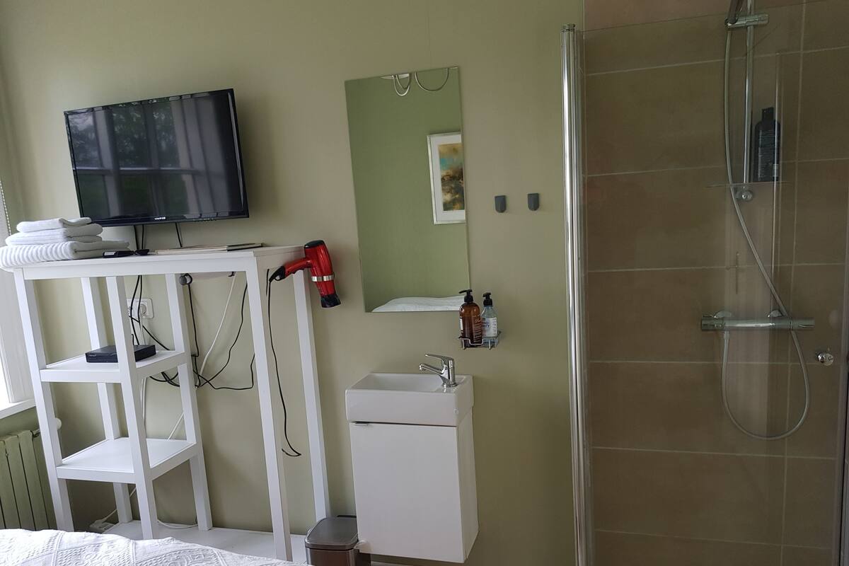 Un dormitorio con una cama, una mesita de noche blanca con un televisor, un secador de pelo y un armario pequeño.