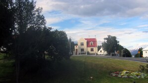 Un espace verdoyant avec une statue, un bâtiment doté d’un toit rouge et une route en arrière-plan.