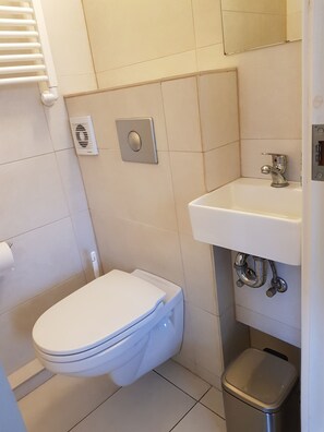 Un baño pequeño y moderno con inodoro, lavamanos y cubo de basura.