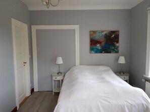 Un dormitorio con una cama grande, dos mesitas de noche con lámparas, una puerta y un cuadro en la pared.