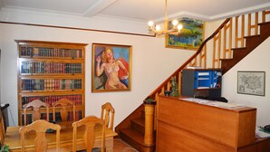 Une bibliothèque avec des étagères, une table à manger, des chaises, un escalier et un tableau accroché au mur.