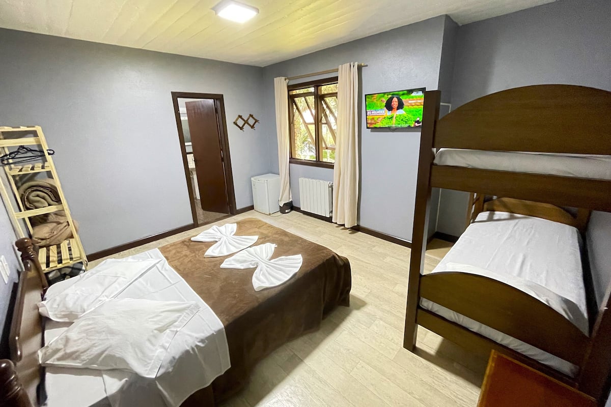 Une chambre avec deux lits, une armoire en bois, un radiateur, une télévision et une fenêtre avec des rideaux.