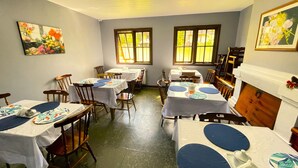 Un espace repas avec des tables dressées pour les repas, des chaises, une cheminée et des œuvres d’art accrochées aux murs.