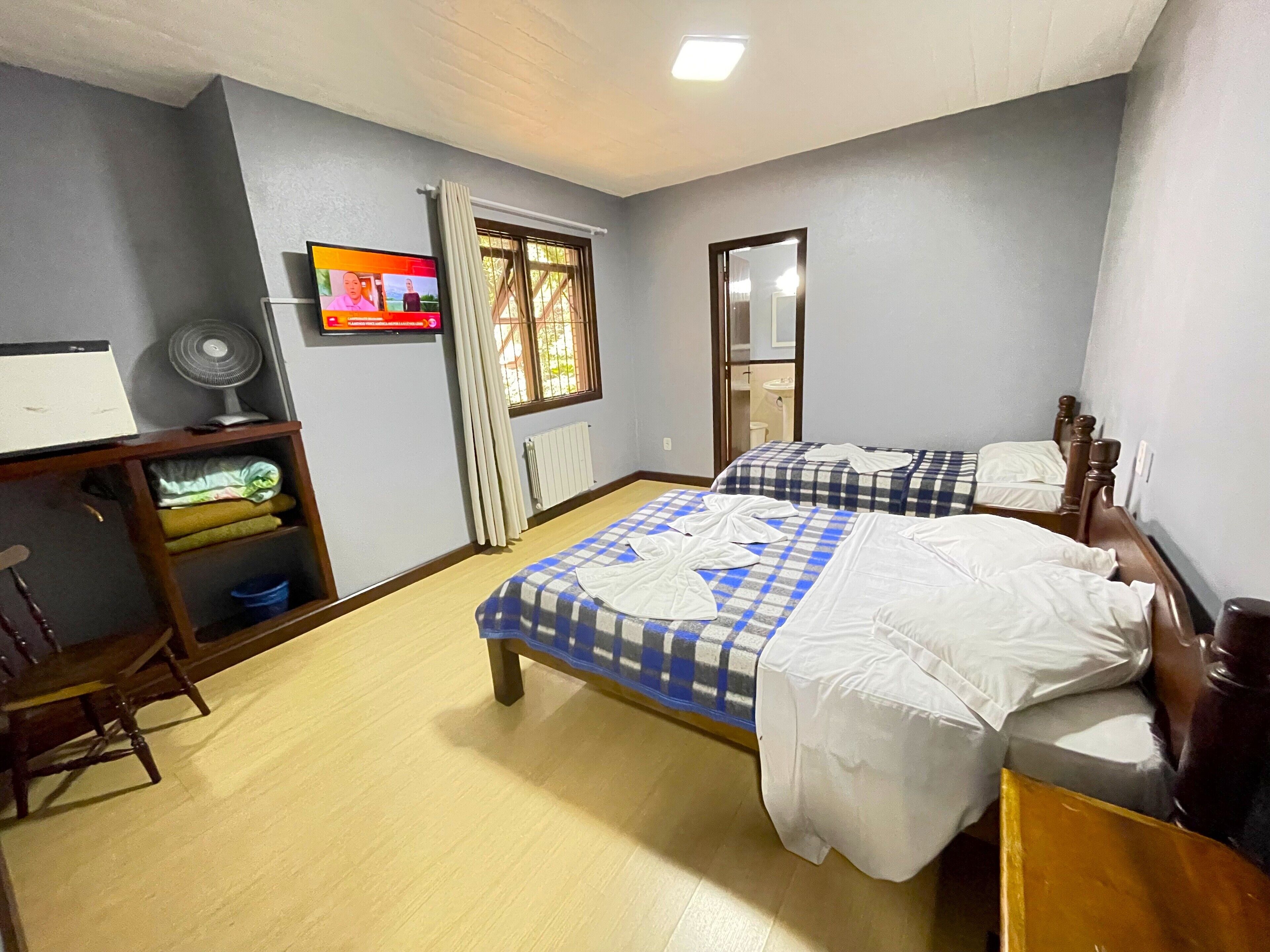 Una habitación con dos camas, un escritorio, una silla, un ventilador y una ventana con cortinas.