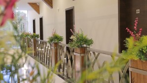 Un pasillo con vigas de madera, plantas en macetas y barandilla de vidrio.