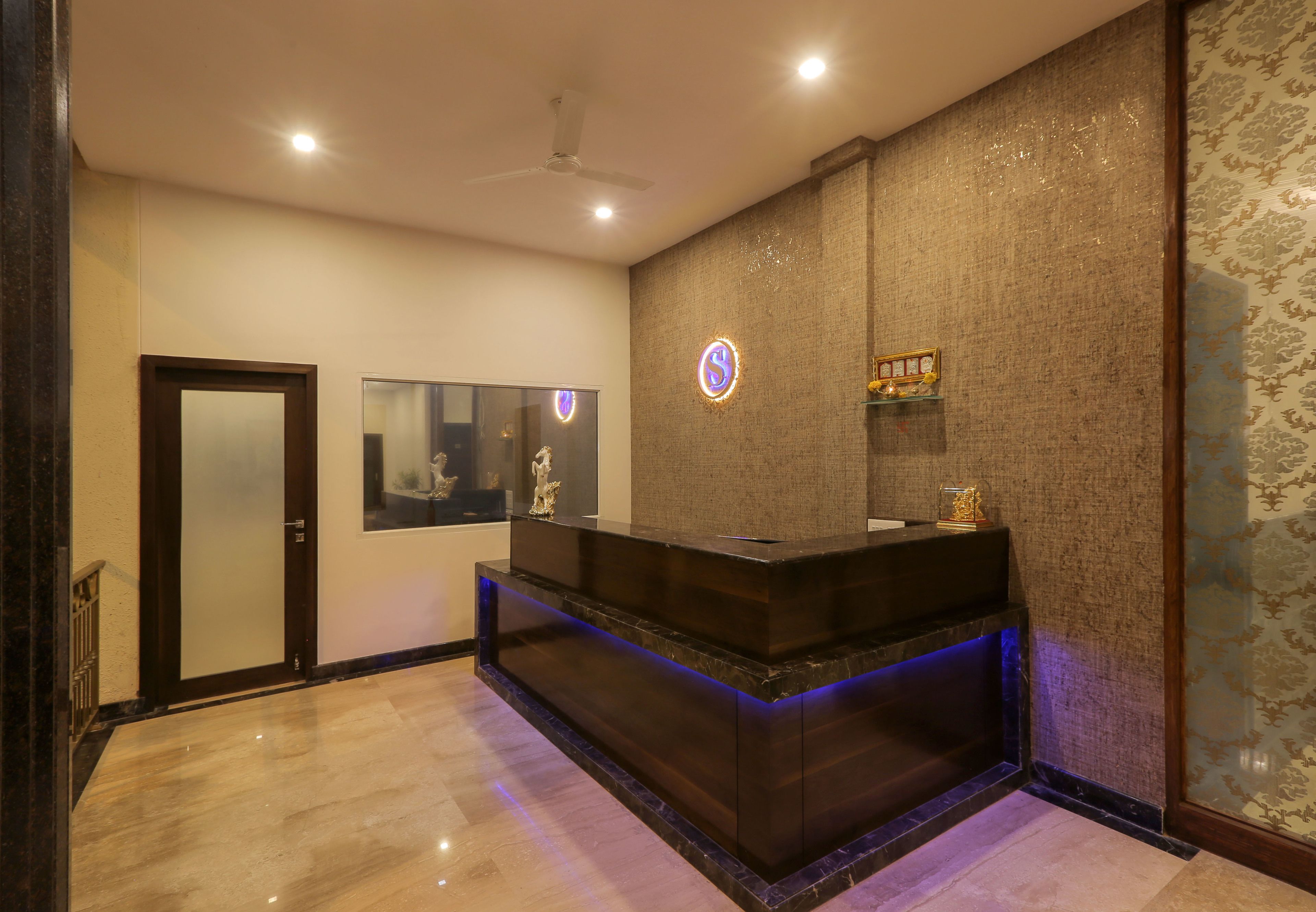 Un área de recepción con piso de mármol, un mostrador oscuro, un ventilador de techo y una pared con textura.