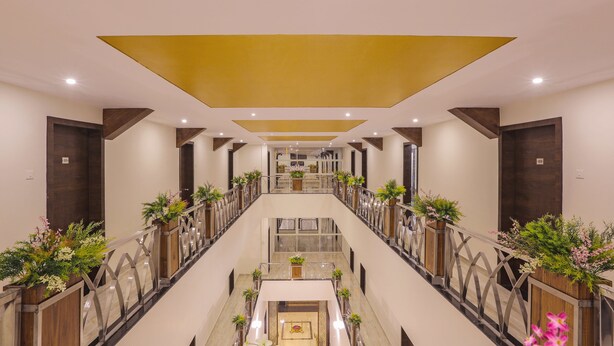 Un pasillo de hotel con una escalera central, puertas de madera y plantas en macetas.