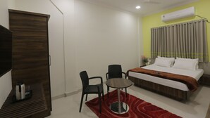 Habitación de hotel con cama, escritorio con silla, una mesita, armario y equipo de aire acondicionado.