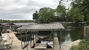 A covered outdoor seating area with a grill and chairs, overlooking a body of water with boats docked nearby.