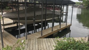 A covered boat dock with a wooden deck, a covered seating area, and a view of a calm body of water.