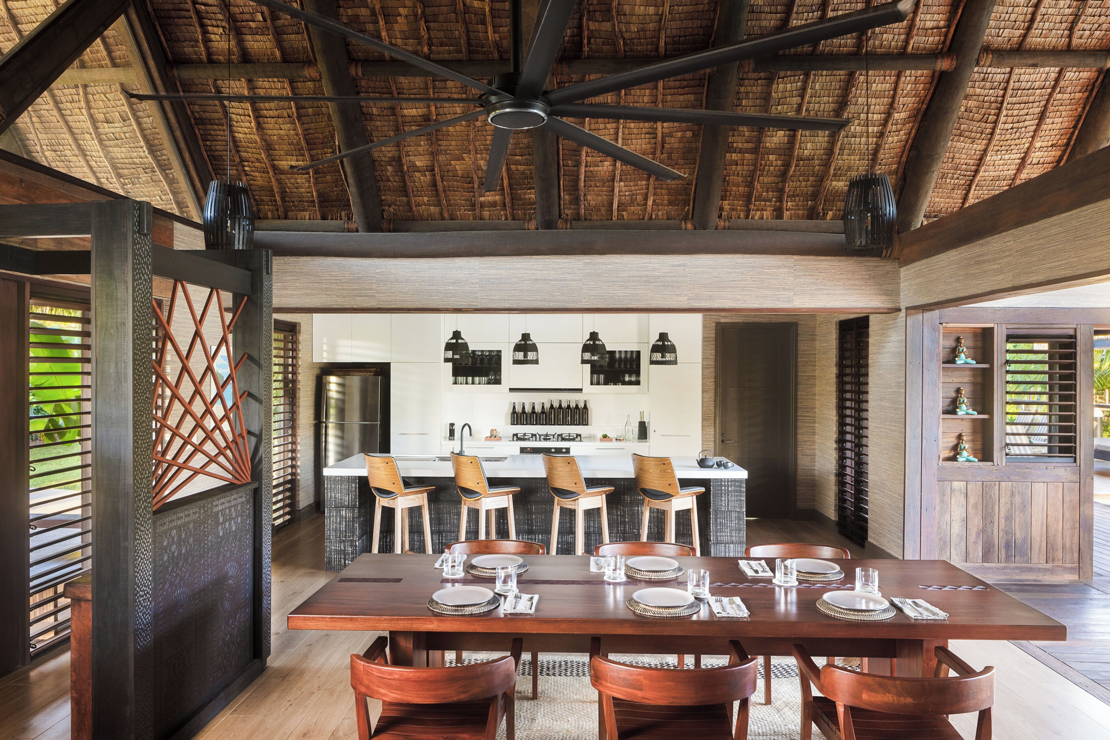 A dining area with a large wooden table set for six, a bar area with bottles, and a ceiling fan.