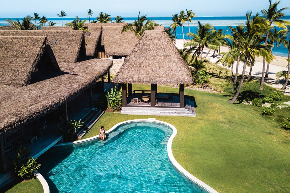 Un resort con piscina, edificaciones de techo de paja y vista al mar.