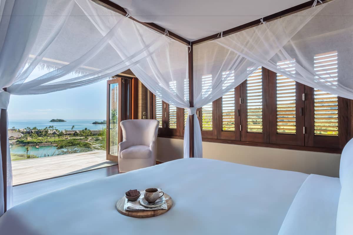Un dormitorio con una cama grande, una silla y vistas a una piscina y el océano.