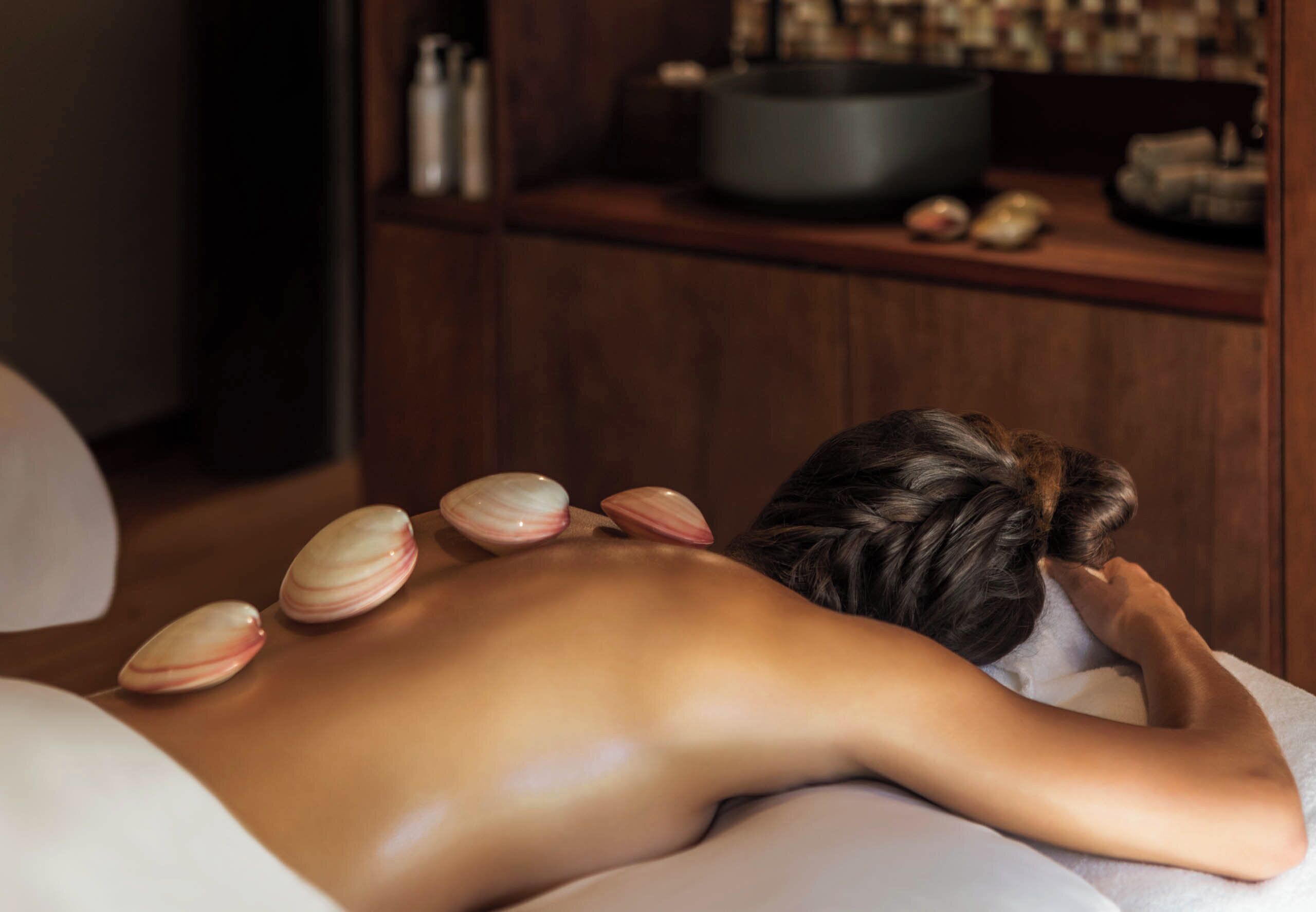 A person receiving a back massage with seashells placed on their back.