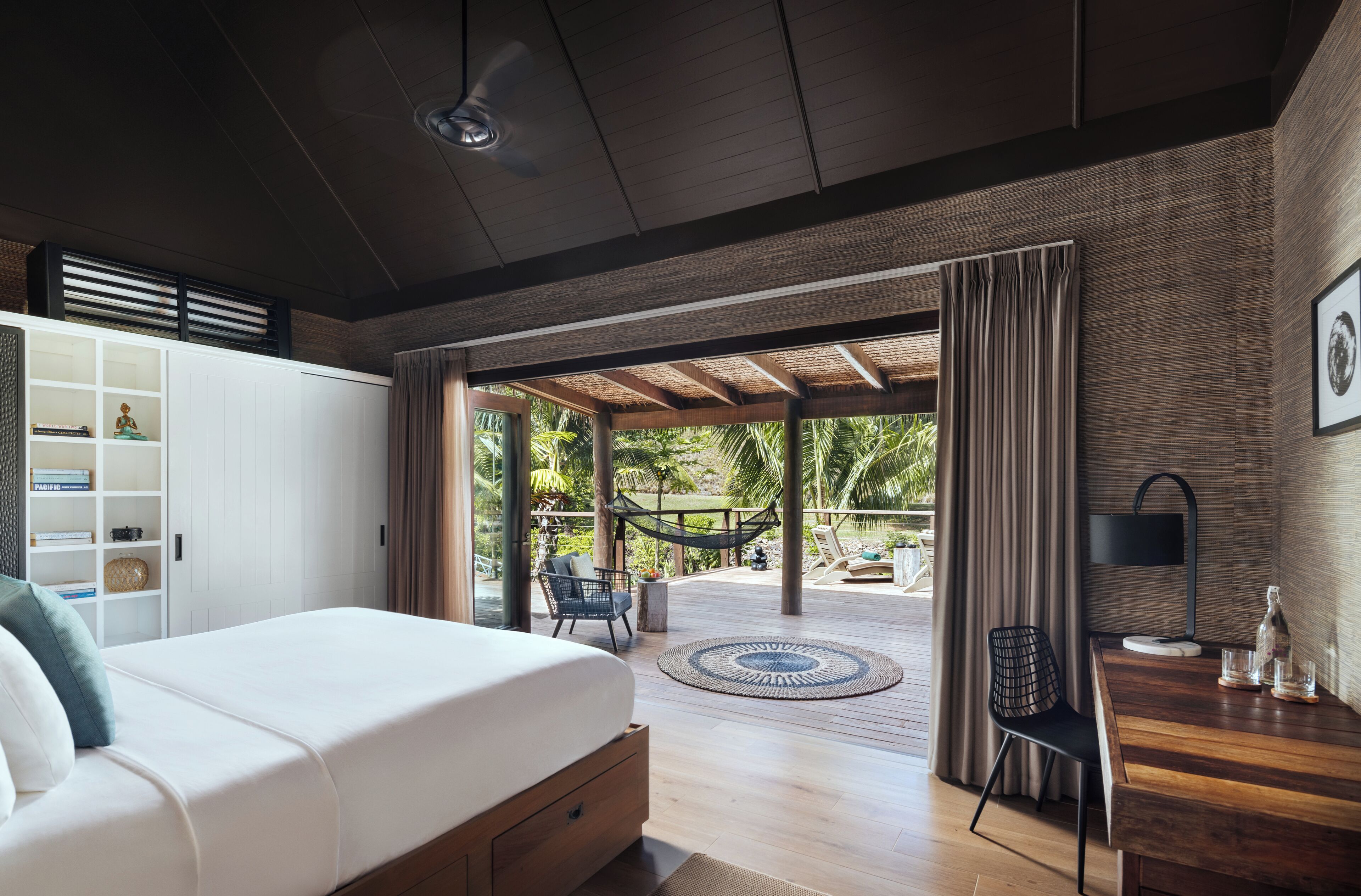 Un dormitorio moderno con una cama grande, un escritorio de madera y vistas a un jardín tropical.