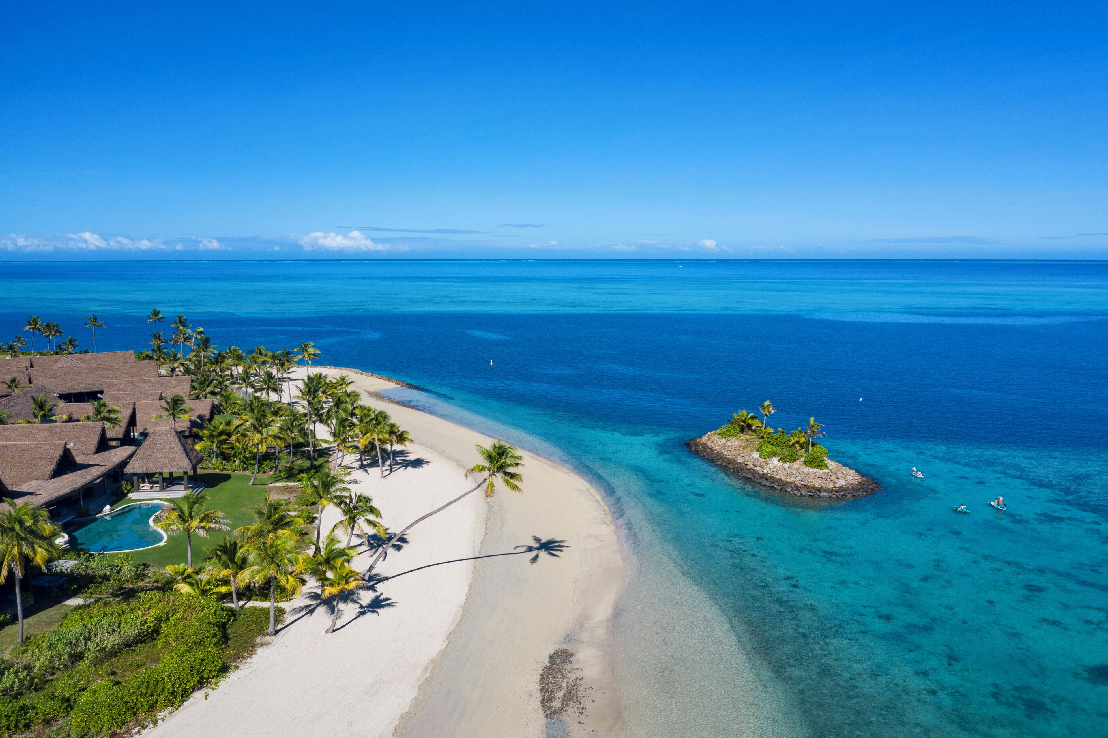A resort with a beach, clear blue waters, and palm trees.