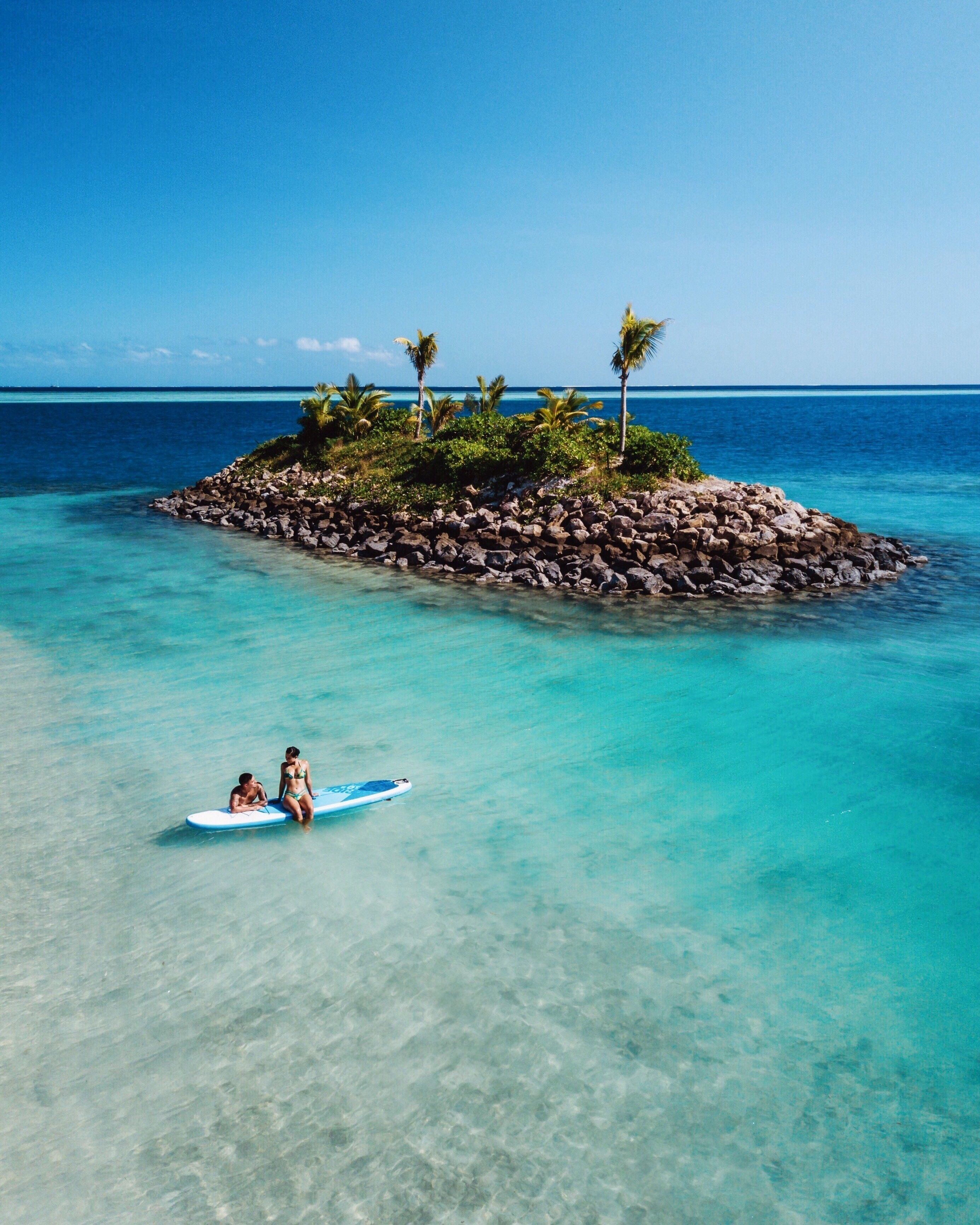 A clear turquoise sea with a small rocky island featuring palm trees.