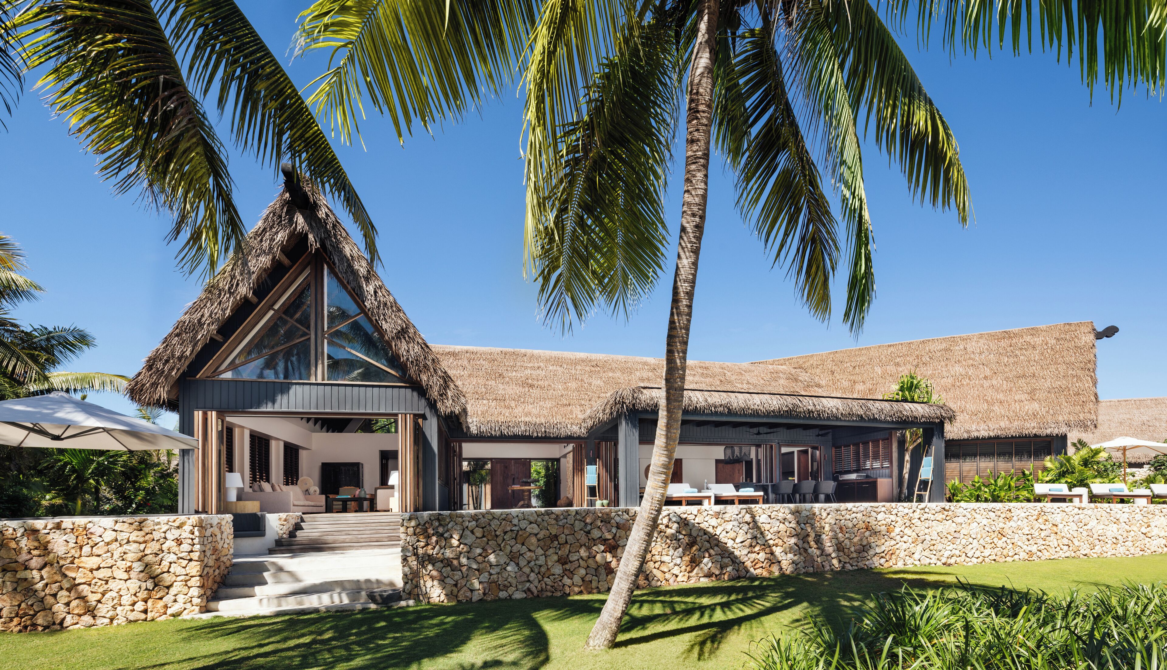 A modern villa with a thatched roof, stone walls, and a pool area.