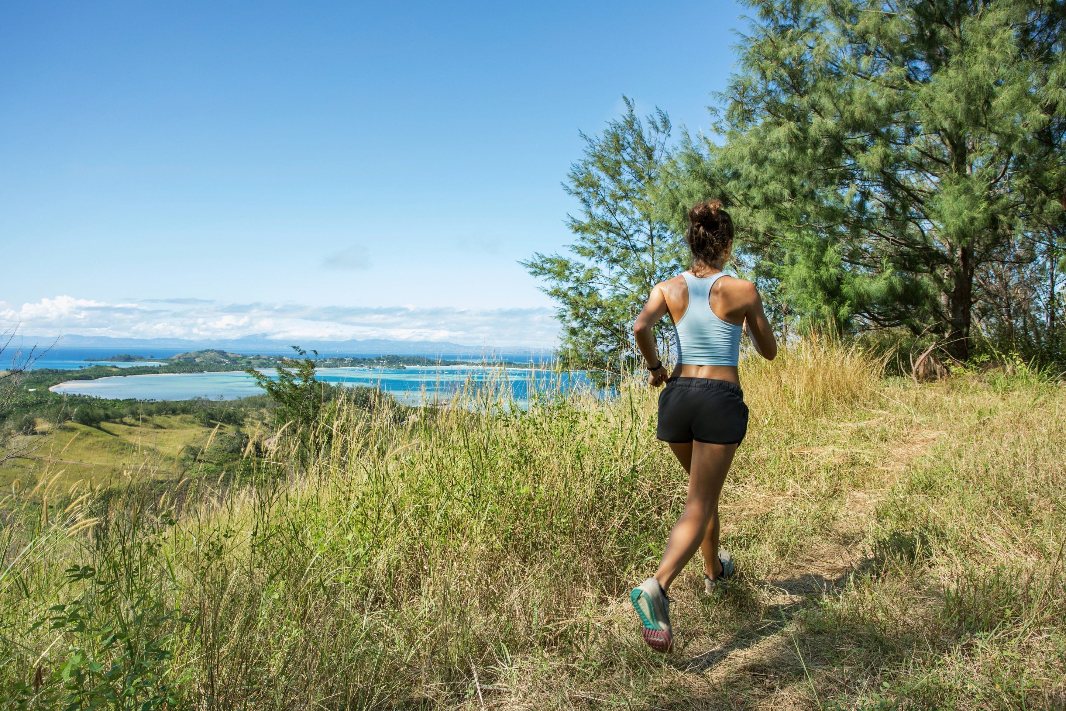 A person jogging on a grassy path with a view of a lake and mountains in the background.