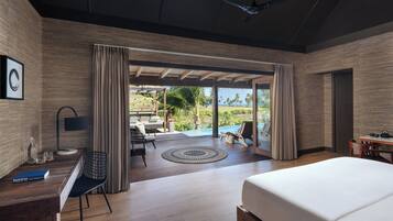 Una habitación de hotel moderna con una cama grande, un escritorio con silla, una mesita y un ventilador de techo, además de vistas al exterior.