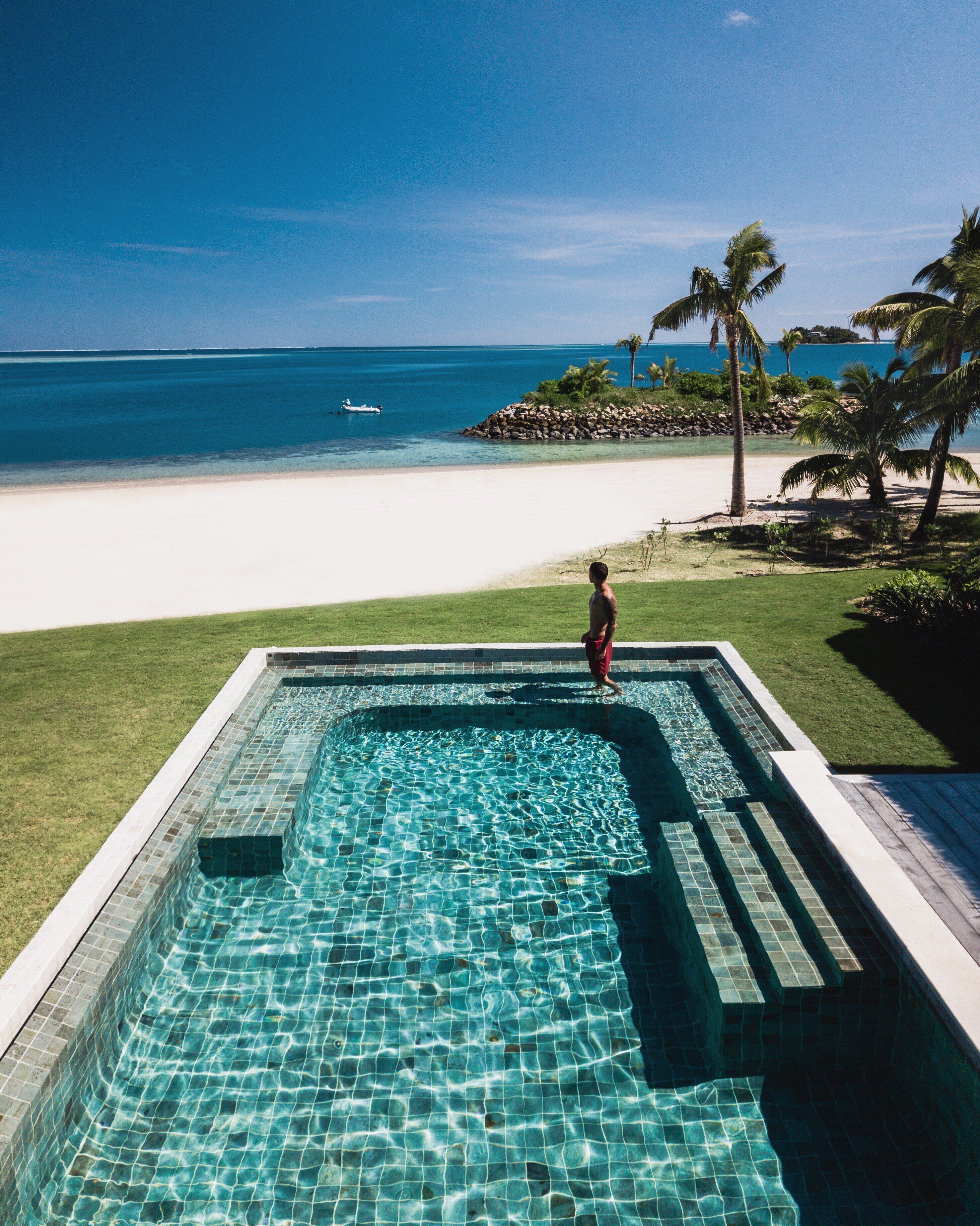 Una piscina con agua azul cristalina, vista a una playa y palmeras.