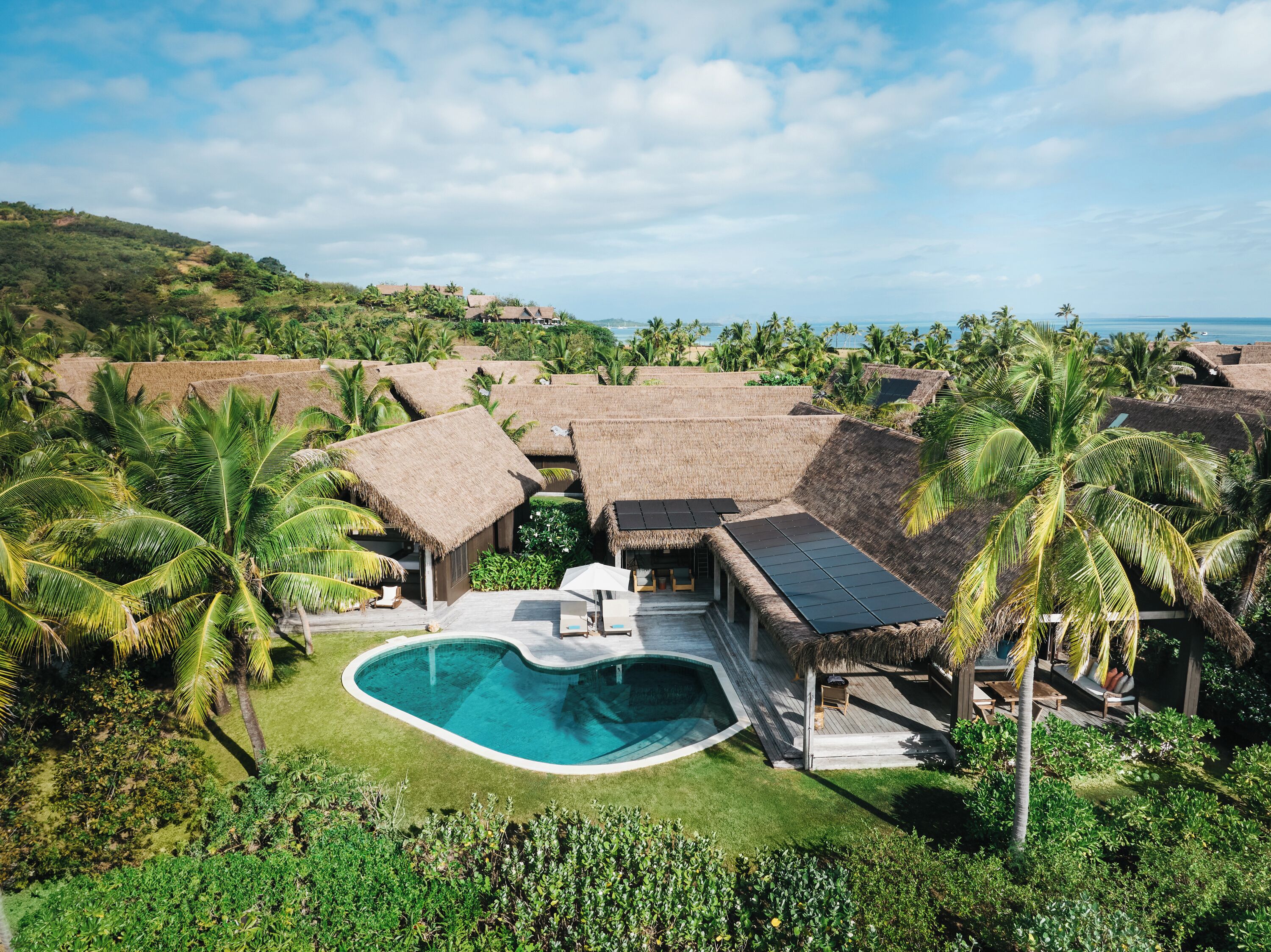 A resort with thatched-roof villas, a swimming pool, and lush greenery.