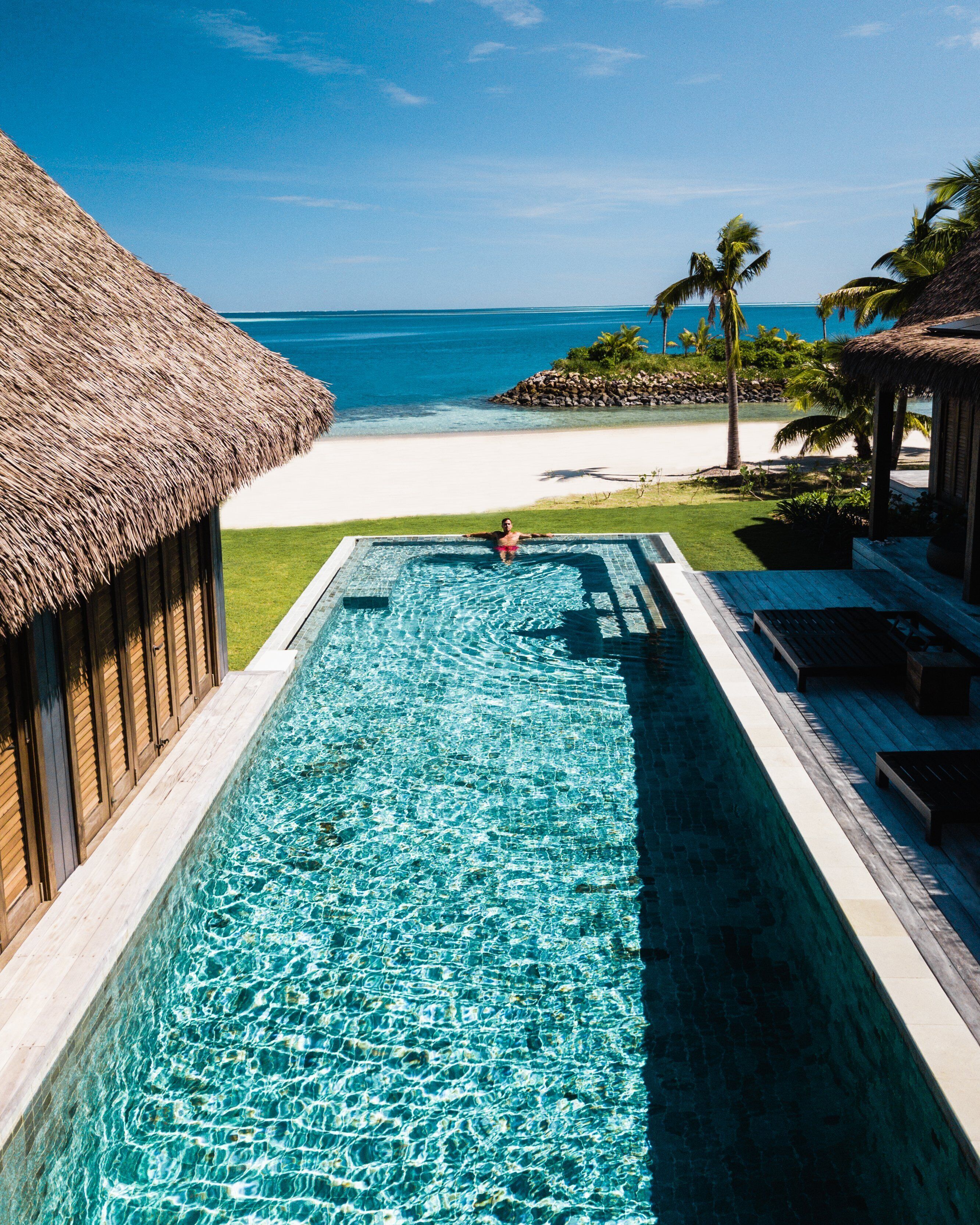 A swimming pool with clear blue water, a beach, and palm trees in the background.