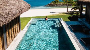 A swimming pool with clear blue water, a beach, and palm trees in the background.
